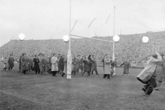 Group of law school students in long coats tossing canes over end zone goal post at Camp Randall Stadium in 1949.