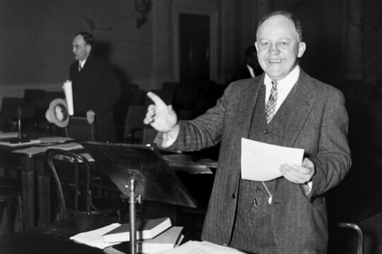 Edwin Witte presenting to the House holding piece of paper while smiling.