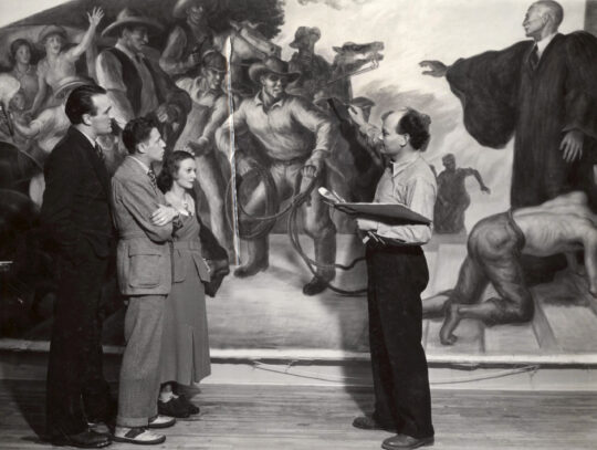 Three people listening to John Steuart Curry speaking about his mural that depicts man fleeing from lawless mob and taking refuge with authority figure wearing long robe.