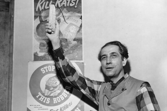 Karl Paul Link standing beside Warfarin advertisements holding up ear of corn.