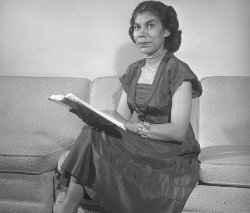 Grayscale portrait of Geraldine Harvey sitting on couch holding an open book in 1950.