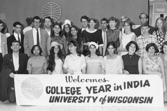 Large group of students standing in three rows posing for photo holding sign that reads, Pan Am welcomes college year in India University of Wisconsin.