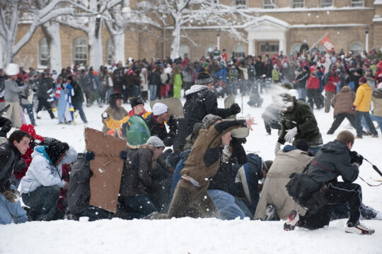 Throng of students defend themselves against snowball attacks on snow-covered Bascom Hill.