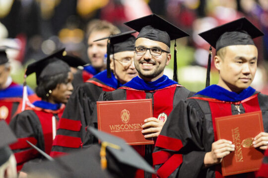 Proud graduates in red and black academic regalia holding their diploma cases at commencement ceremony.