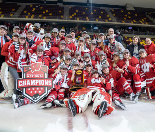 UW Badgers women's hockey team and coaching staff celebrating their 2023 National Championship victory on the ice.
