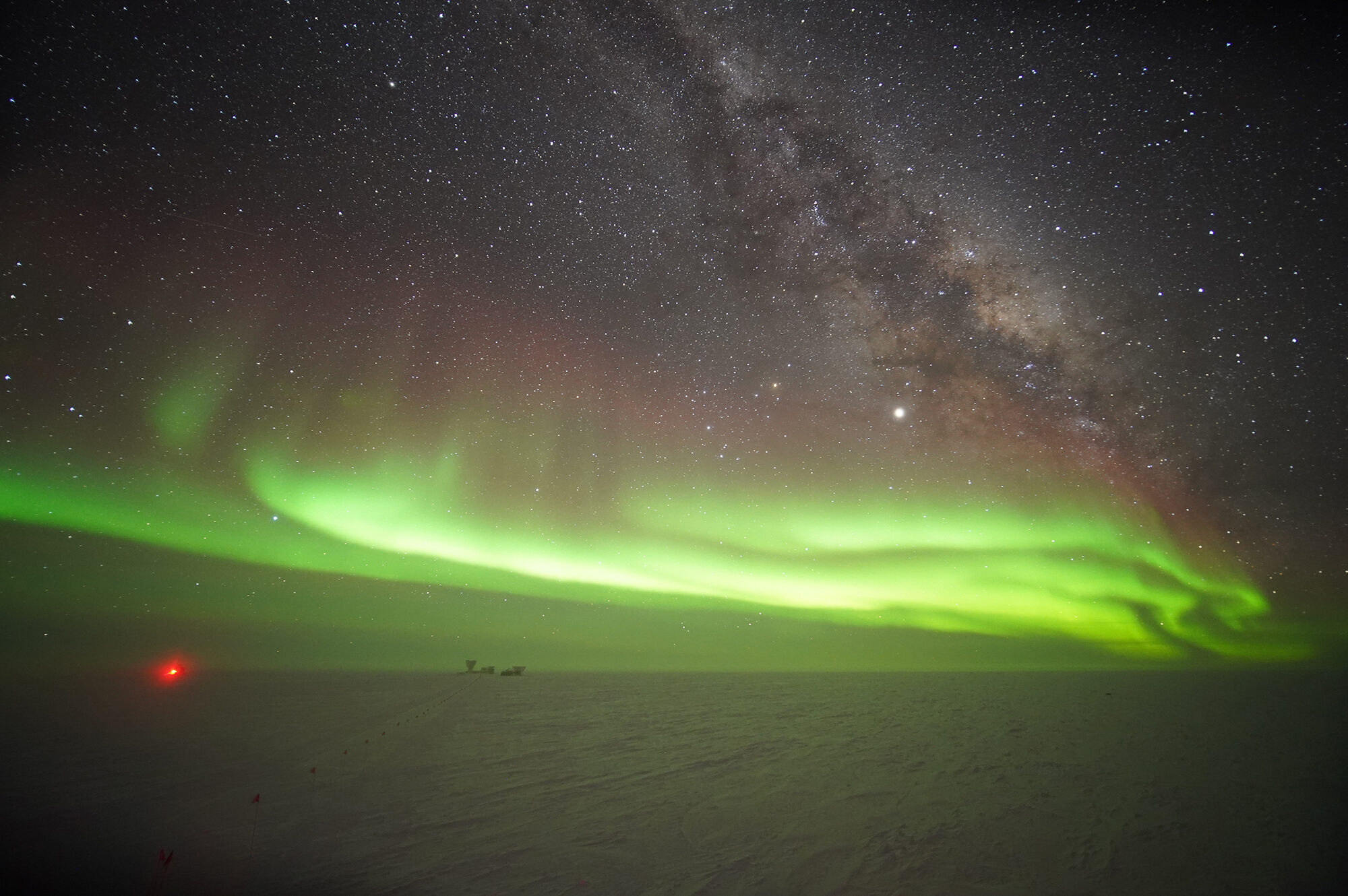 Green aurora borealis lights across starlit sky at south pole.