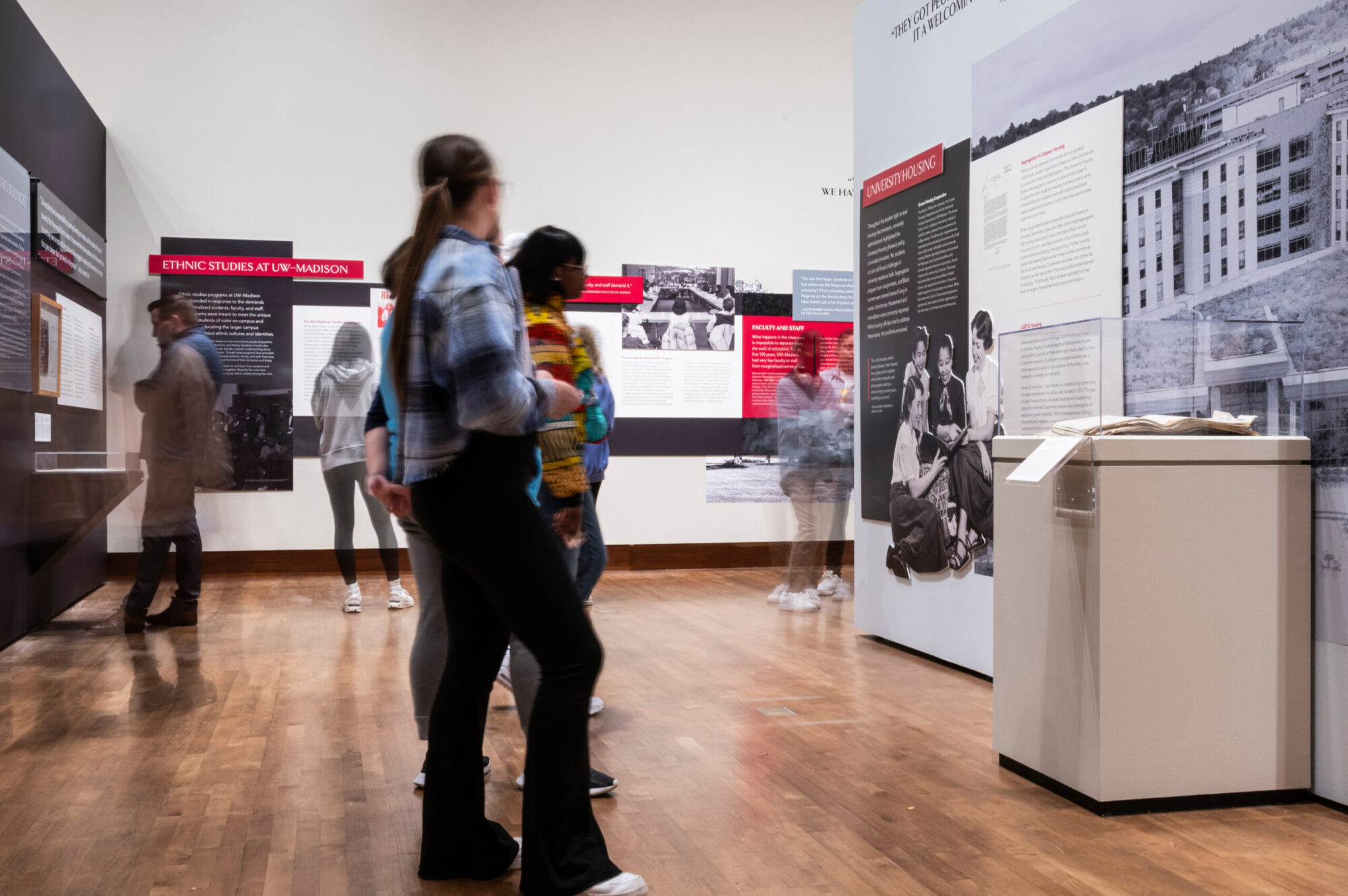 Students and visitors viewing curated artifacts and wall panels at Sifting & Reckoning: UW–Madison’s History of Exclusion and Resistance exhibit.