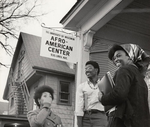 Four students standing on porch below small sign that reads, The University of Wisconsin–Madison Afro-American Center at 935 Univ Avenue.