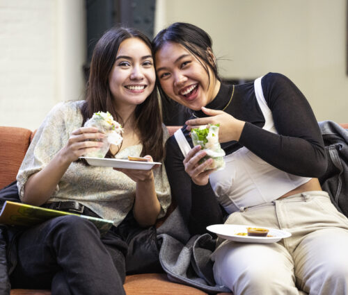 Two students smiling while enjoying spring rolls.