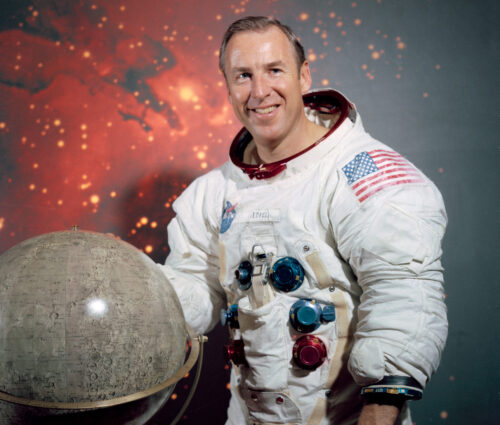 Portrait of astronaut James Lovell standing beside model of moon.
