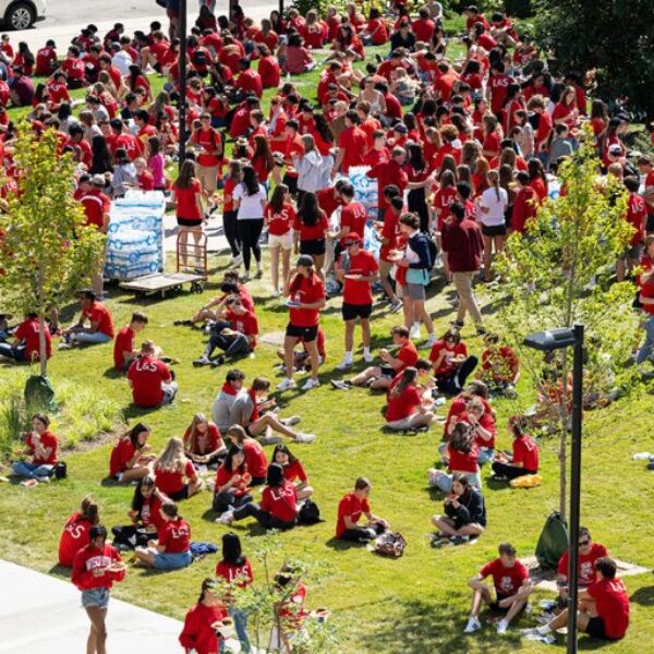 Large group of students in red gathered on outdoor green space.