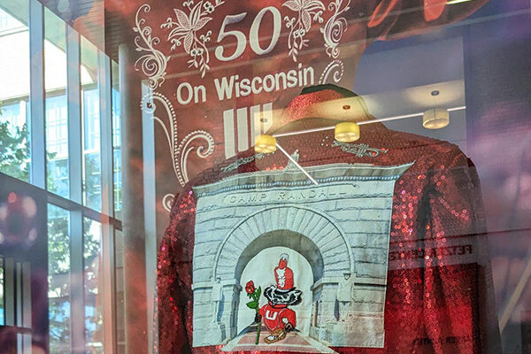photo of a red sequin jacket with a large patch on the back in a display window with a large photo behind and light reflecting off the window.