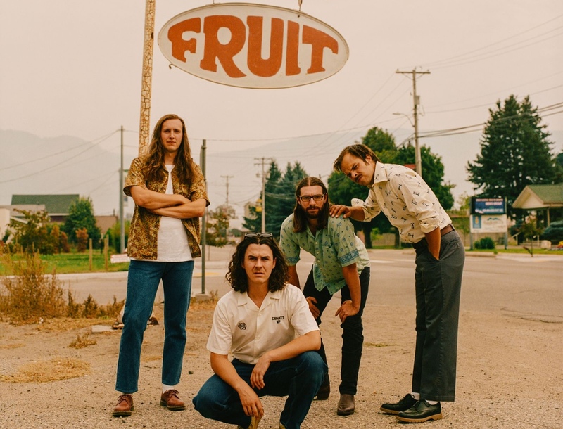 Members of Peach Pit standing along a roadside in front of sign that reads "fruit"