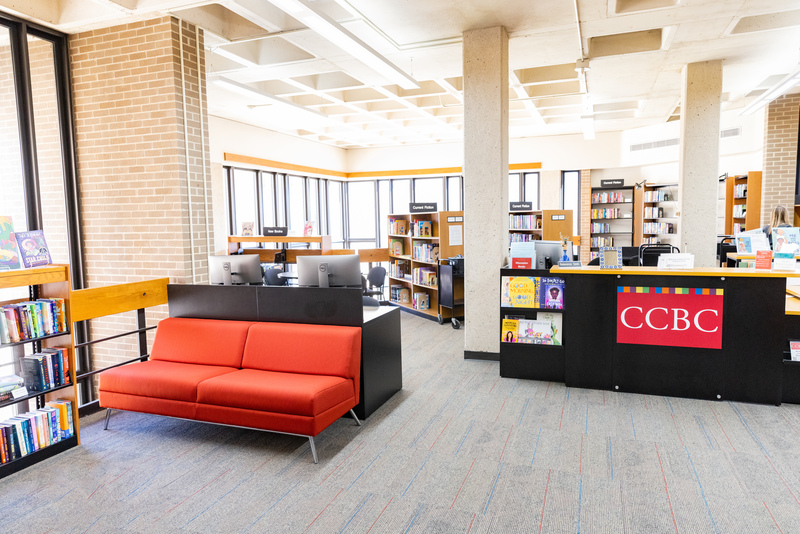 An image of the CCBC, comprised of bookshelves, a welcome desk, and a red couch.