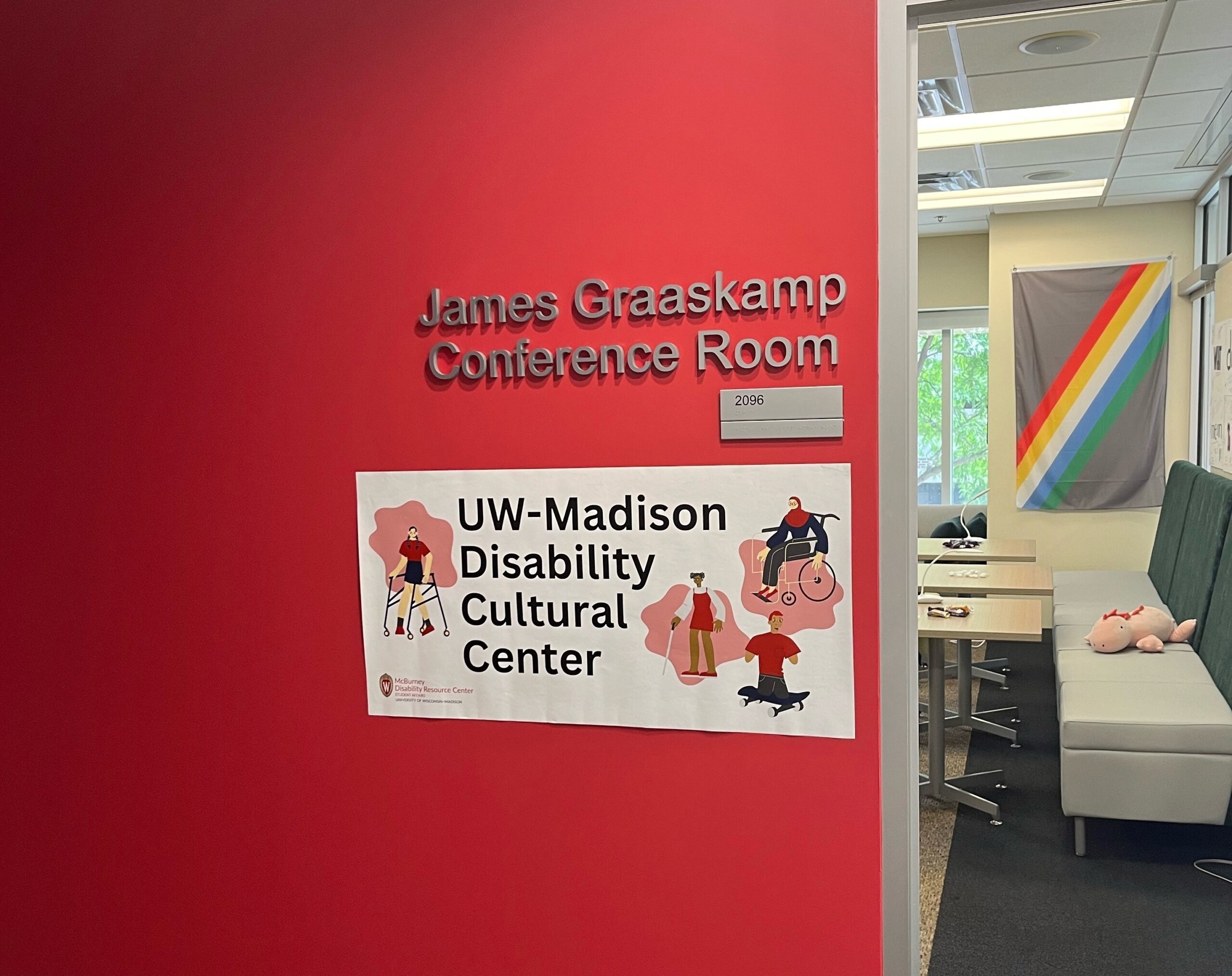 Entrance to the Disability Cultural Center with sign fixed to red wall that reads, UW–Madison Disability Cultural Center.