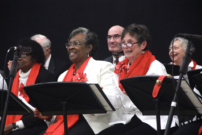 A photo of members of The Amazing Grace Chorus singing, dressed in red, black, and white.