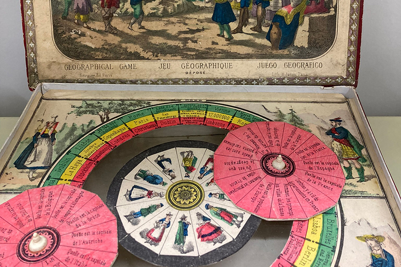 A photo of an old, colorful board game, featuring wheels and drawings of historic individuals.