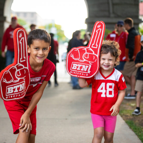 A photo of two children decked out in badger red, holding Big Ten Network foam fingers outside Camp Randall arch.