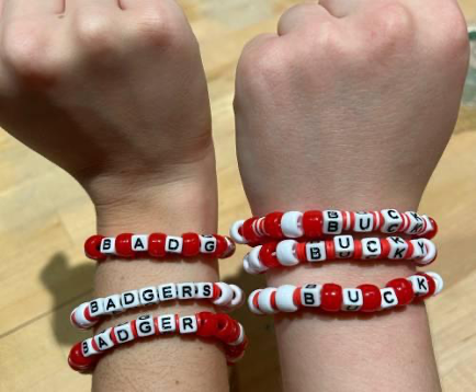 Two arms outstretched wearing red and white bead bracelets that read Bucky and Badger.