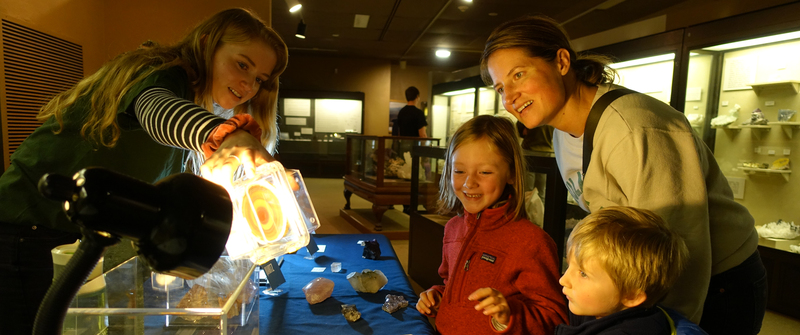 Visitors gaze at an brown and cream colored agate slab being backlit and held by a museum volunteer.