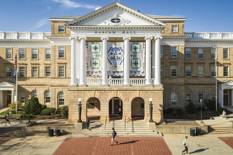 A photo of the white seed by seed banners with blue, pink, green, and yellow, adorning Bascom Hall.