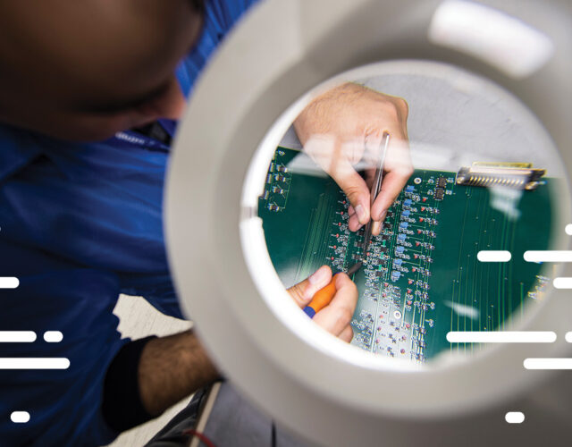 Magnified look at person using handheld tools working on green circuitboard.