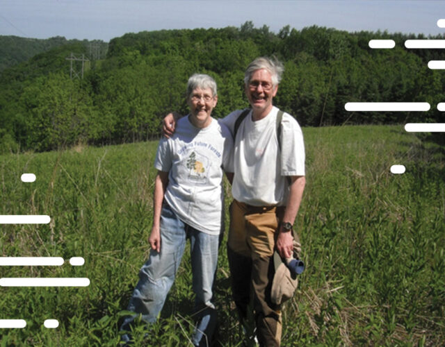 Two people posing for picture standing outdoors in field of tall grass.