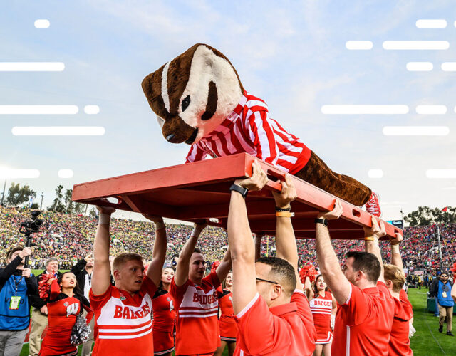 Bucky Badger doing pushups on red board held high in air by members of UW–Madison's Spirit Squad.