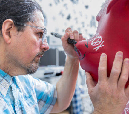 A man stands face-to-face with the Bucky Badger statue as he paints details on it.
