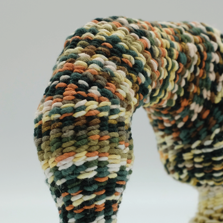 photo of a woven textile sculpture in white, green, red, and yellow.