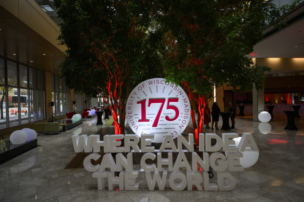 3-D display stating, “Where an idea can change the world” in front of circular 175th anniversary logo positioned between uplight indoor trees.