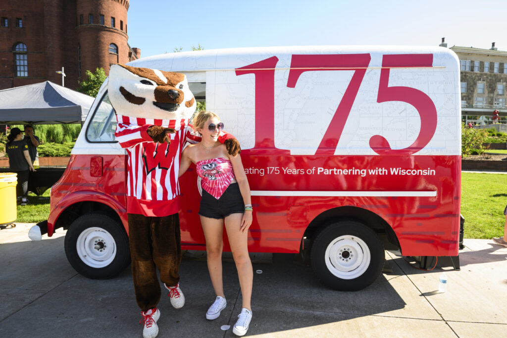 Person posing with Bucky Badger in front of red and white truck decorated for the 175th anniversary.