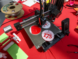 175 Open House - 3-D Printing Machine 3-D printing machine on red table creating 175-themed medallions.