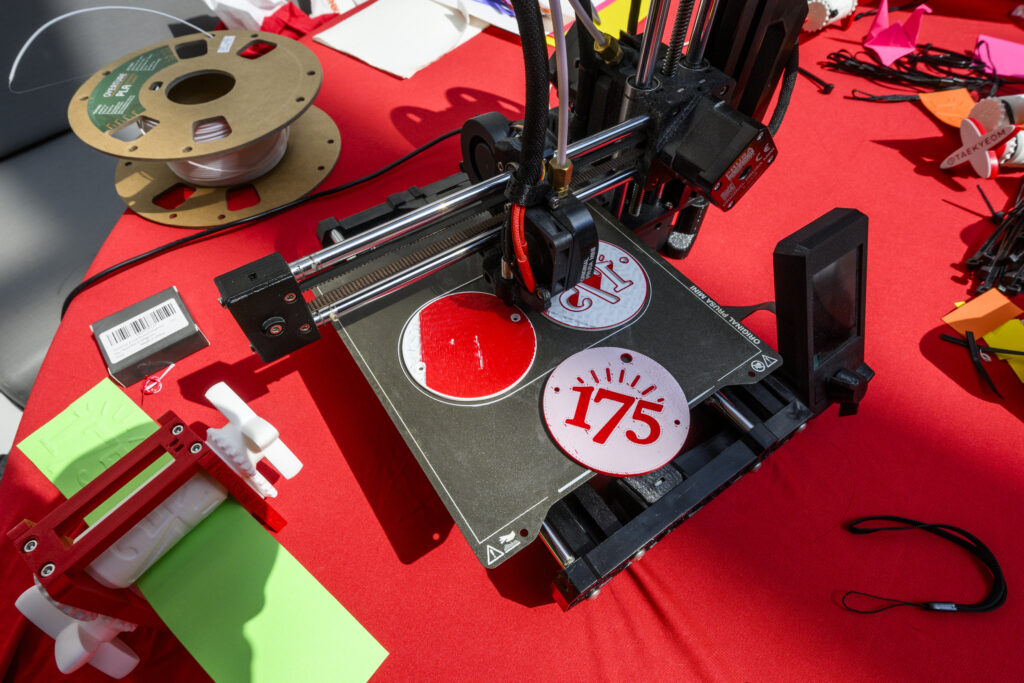 3-D printing machine on red table creating 175-themed medallions.