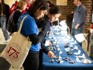 175 Open House - Geology Museum Two people looking at small rocks, minerals, and fossils on table available for purchase.
