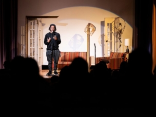 175 Open House - Spoken Word Undergraduate student on stage performing spoken-word piece to crowd of people in foreground.