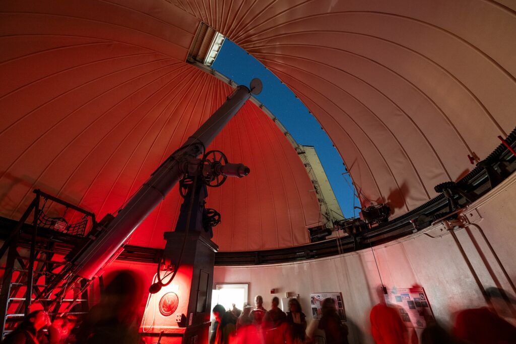 Observatory telescope peering through dome-slit during evening stargazing event.