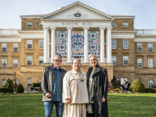 Ho-Chunk Banners Celebration Three people posing for photo in front of Ho-Chunk banners hanging between building columns of Bascom Hall on autumn morning.