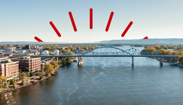 Arched bridge passing over river with city buildings on one side and trees on other side overlaid with red bursts.