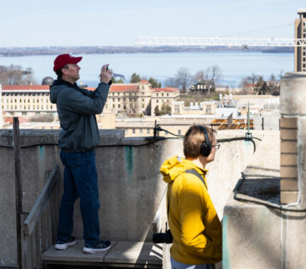 Some people take cell phone photos from the top of a tall building, the landscape in the background.